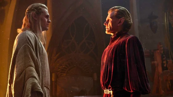 L'acteur Charles Edwards dans le rôle de Celebrimbor, elfe aux oreilles pointues, face à un autre elfe de profil dans une salle ornée baignée de lumière dorée, scène de la saison 3 de The Rings of Power