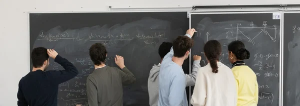 Six étudiants vus de dos, quatre garçons et deux filles, travaillant ensemble devant un grand tableau noir couvert d'équations mathématiques complexes, de trigonométrie et de schémas
