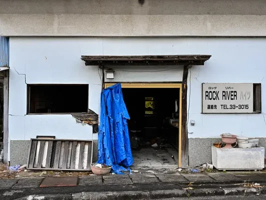 Un izakaya abandonné depuis la catastrophe de 2011 près de la gare de Futaba, à Fukushima, avec une bâche bleue recouvrant l'entrée et l'enseigne « ROCK RIVER »