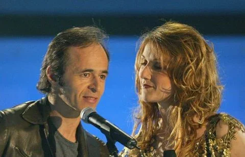Jean-Jacques Goldman et Céline Dion se tenant côte à côte devant un micro lors d'un événement sur scène, évoquant une collaboration