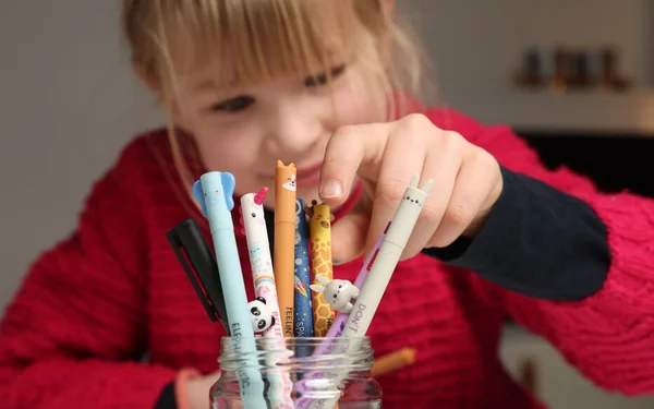 Un enfant blond en pull rouge plongeant la main dans un bocal rempli de stylos colorés à bouchons en forme d'animaux, les célèbres stylos Legami