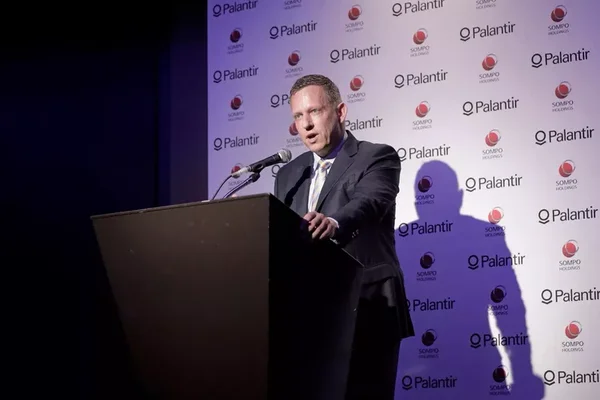 Peter Thiel, co-fondateur et président de Palantir Technologies, s'adressant à un micro derrière un pupitre lors d'une conférence de presse à Tokyo, devant un décor répétant les logos de Palantir et Sompo Holdings