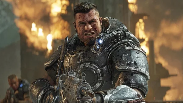 Soldat lourdement blindé de Gears of War: E-Day le visage ensanglanté, serrant les dents en tenant son arme dans un environnement dévasté
